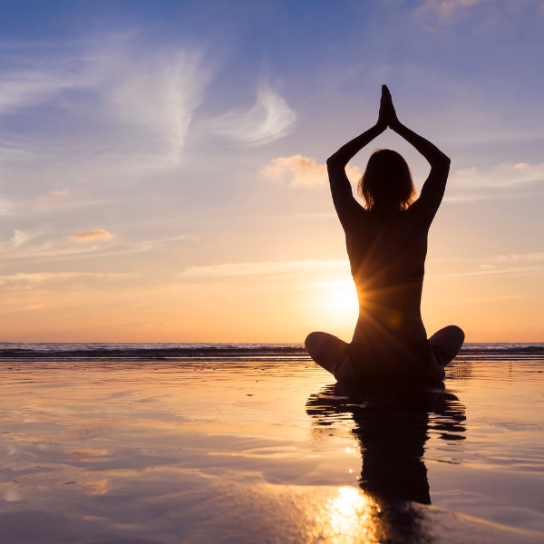 Woman practicing yoga meditation on the beach during sunrise, promoting physical well-being at Iyali Chennai.