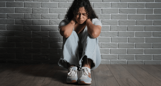 Woman sitting on the floor holding her head in distress, illustrating symptoms of a panic attack addressed at Iyali Counselling