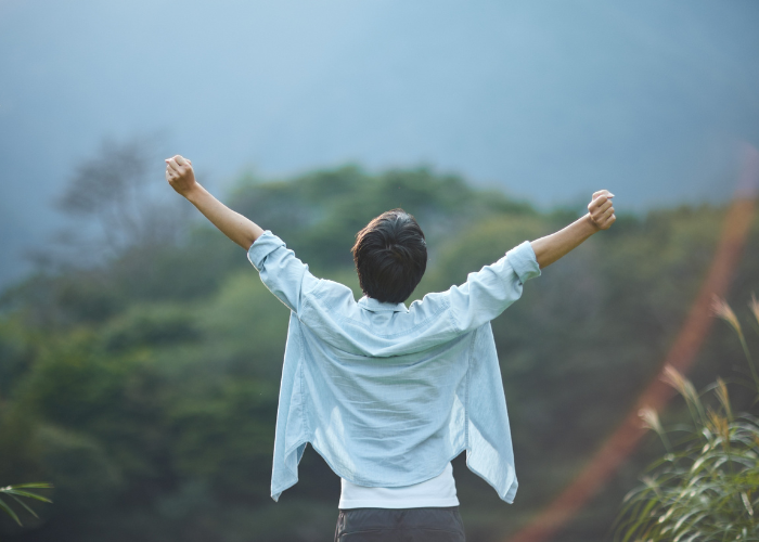 Person standing outdoors with arms raised toward the sky, symbolizing confidence, clarity, and personal growth.