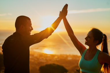 Man and woman high-fiving outdoors during a sunrise fitness session.